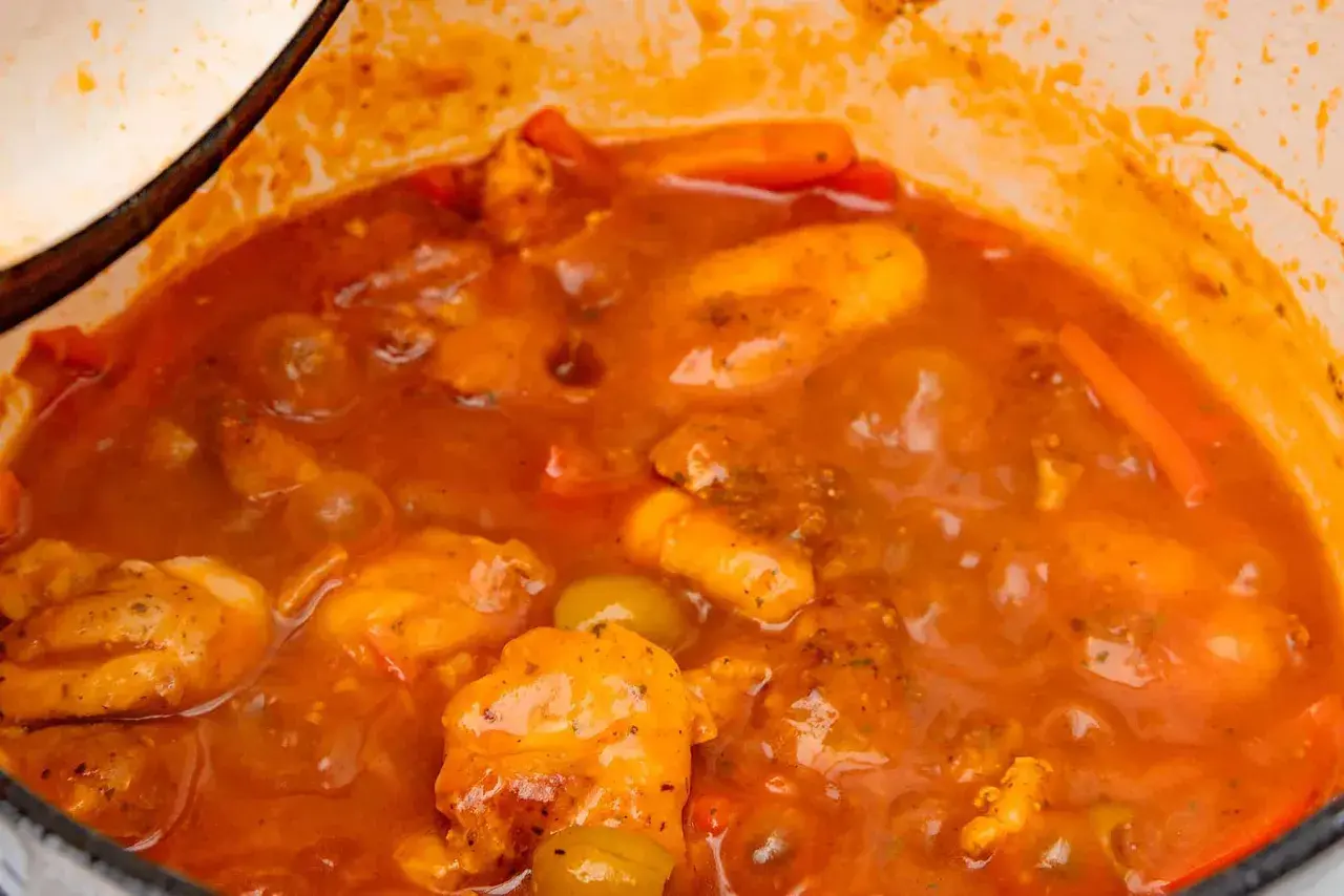 Guiso casero de pollo con tomate, zanahoria y aceitunas verdes, cocinado a fuego lento en una olla.