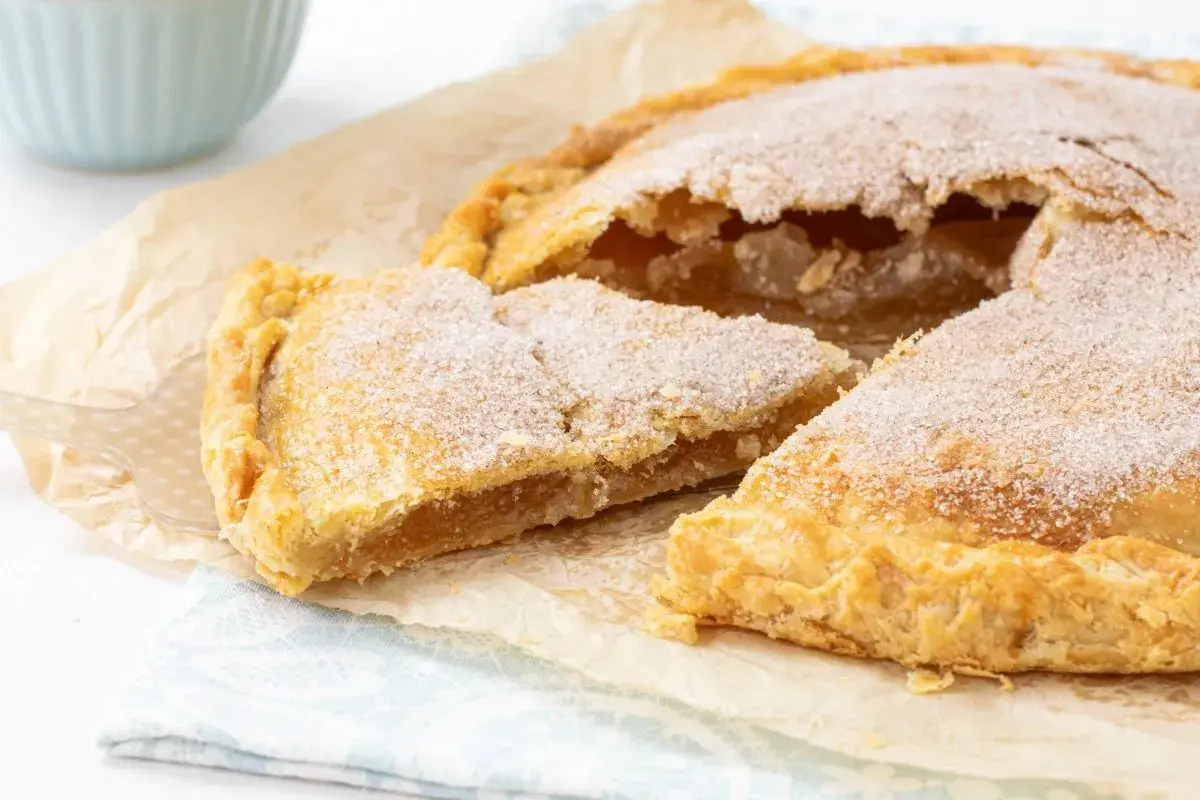 Un delicioso pastel cordobés, espolvoreado con azúcar, con una porción cortada mostrando su relleno dorado.