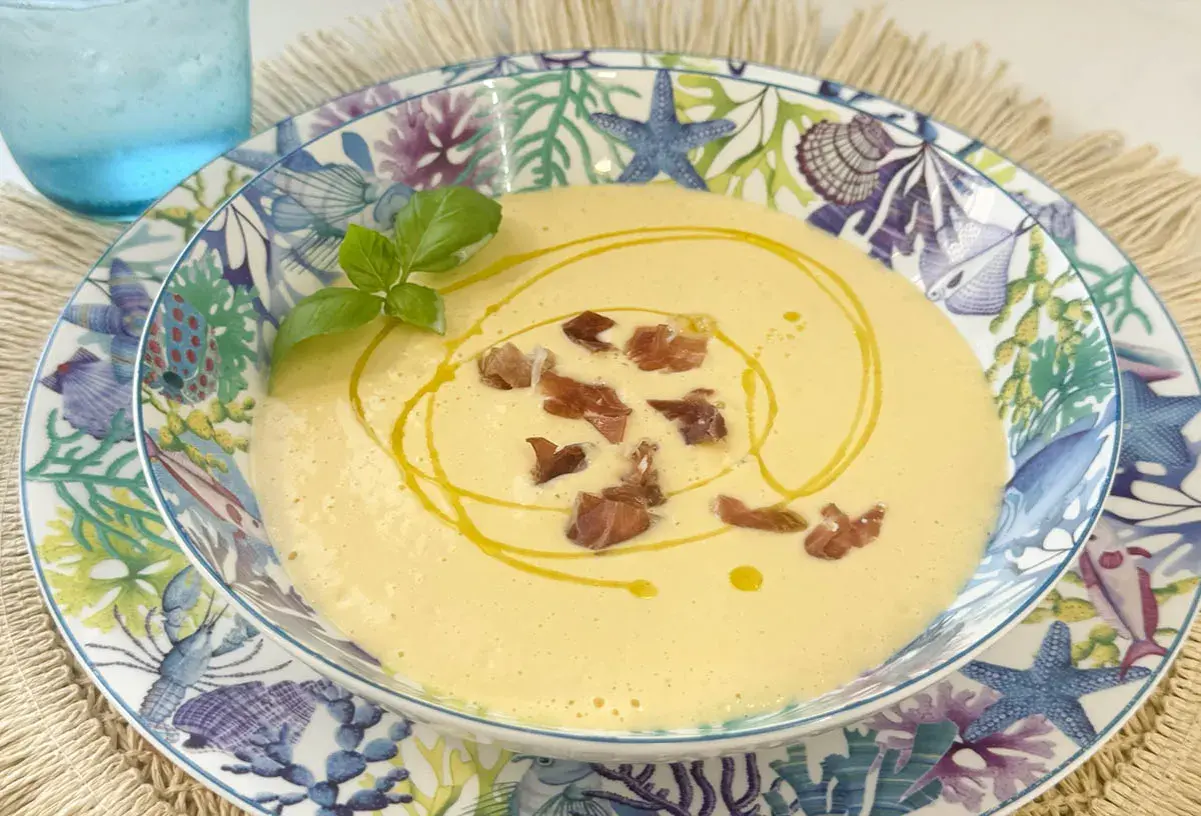 Deliciosa crema de espárragos, coronada con crujientes trocitos de jamón y un hilo de aceite de oliva. Servida en un plato con motivos marinos.