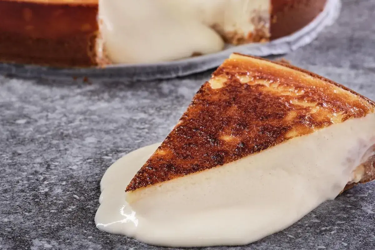 Una porción de tarta de queso cremosa, con la base dorada y el relleno blanco, se desliza sobre una salsa de queso.