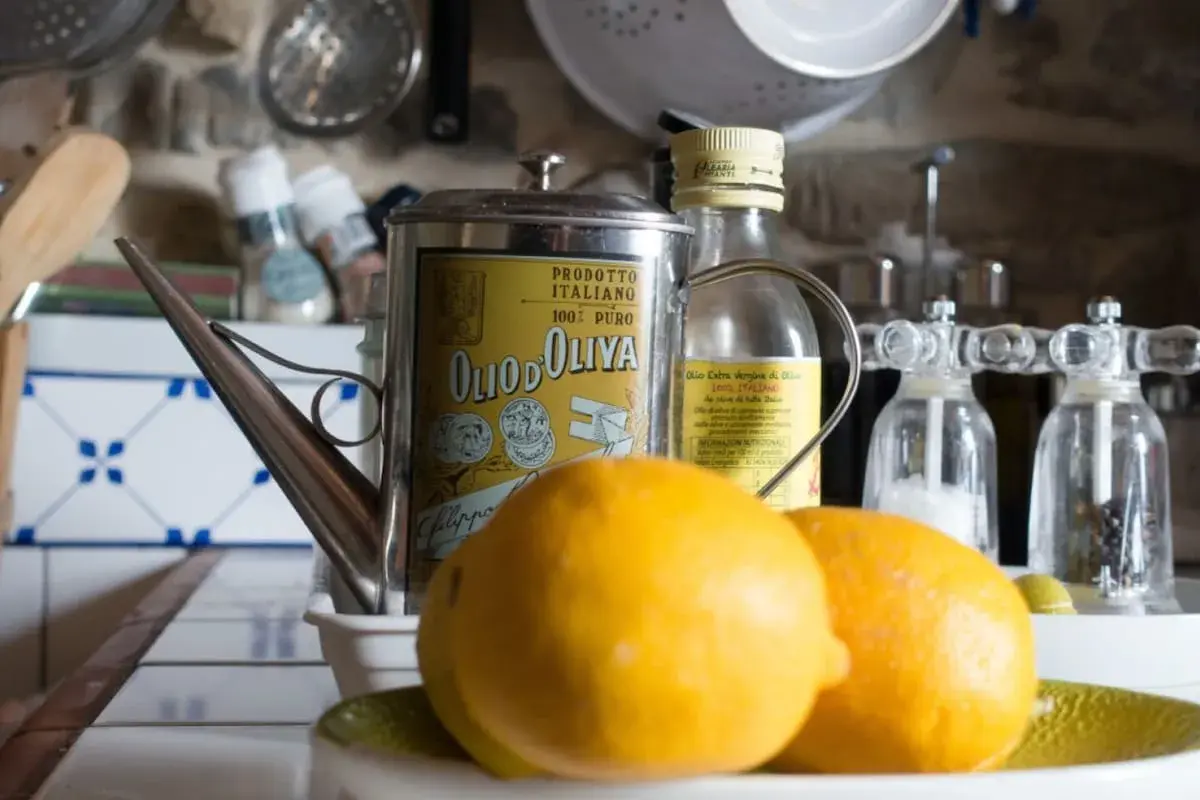 Aceite de oliva y limón para que sirve: una lata vintage de aceite de oliva italiano, limones frescos y molinillos de sal y pimienta en una cocina rústica.