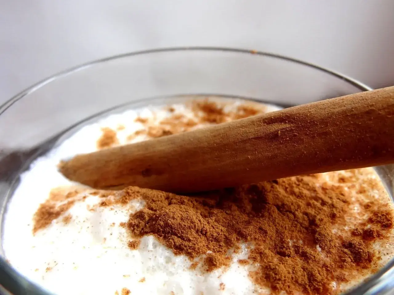 Vaso de leche merengada con canela en polvo y una rama de canela.