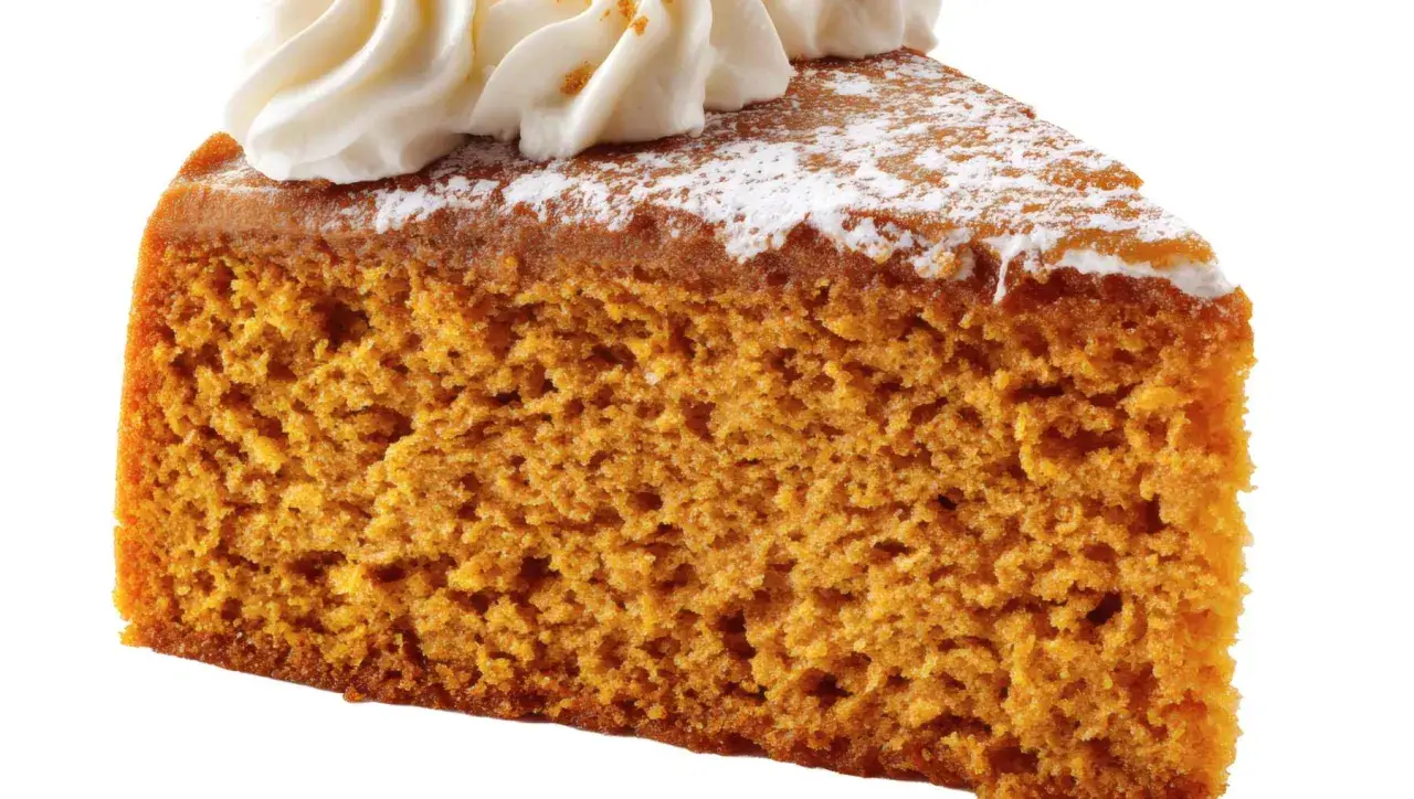 Rebanada de bizcocho de calabaza esponjoso, cubierto con crema batida y espolvoreado con azúcar glas.
