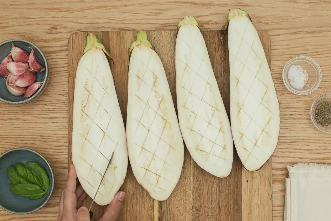 Berenjenas cortadas a la mitad, listas para ser rellenas. A su lado, ajos, albahaca, sal y pimienta.