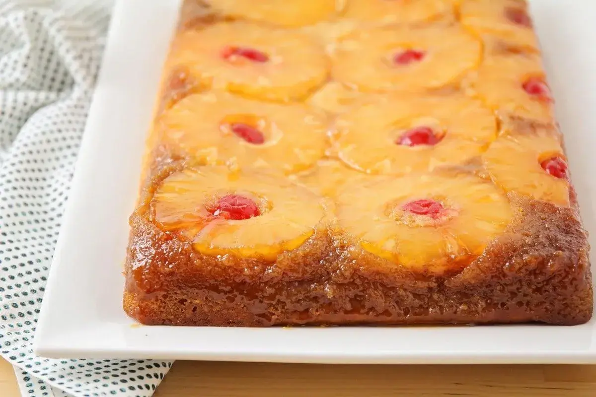 Tarta de piña dorada y brillante, con rodajas de piña caramelizada y cerezas rojas en cada centro. Un postre casero irresistible.