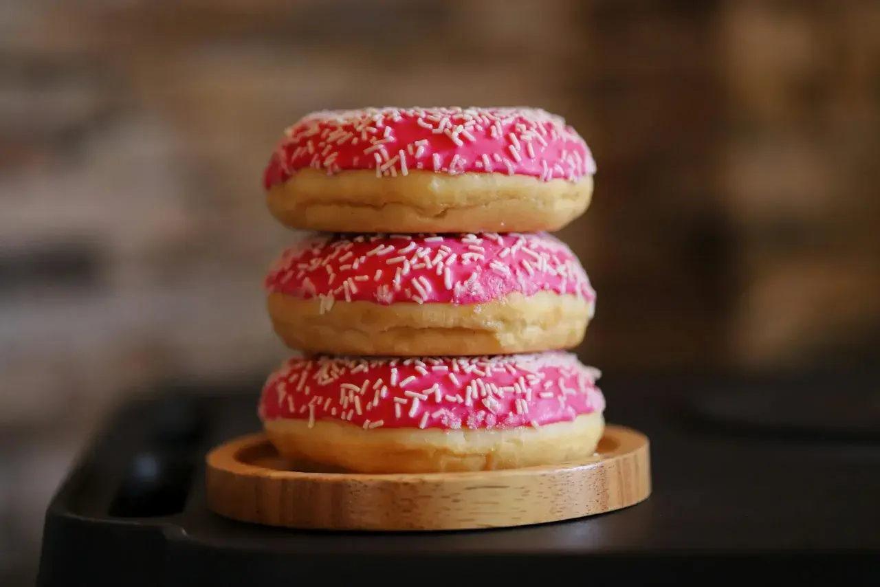 Tres deliciosos donuts caseros apilados, cubiertos con glaseado rosa brillante y chispas blancas.