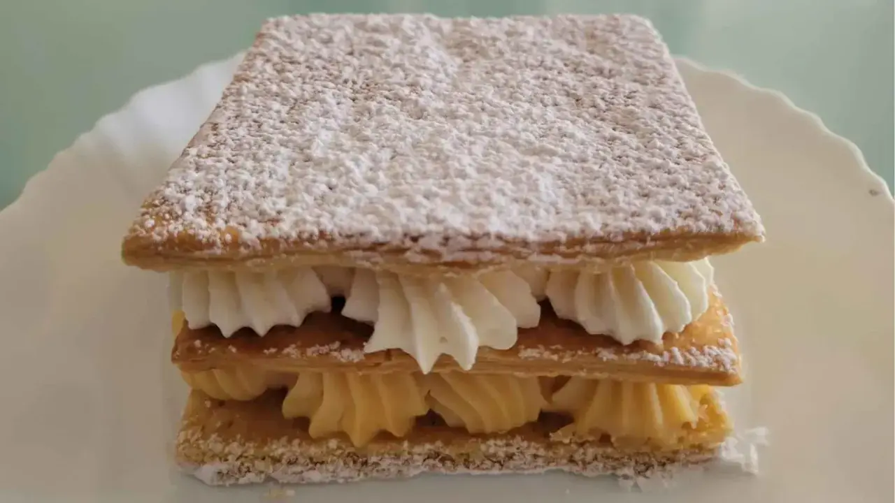 Delicioso milhojas de crema, con capas crujientes de hojaldre y rellenos de crema pastelera y nata montada, espolvoreado con azúcar glas.