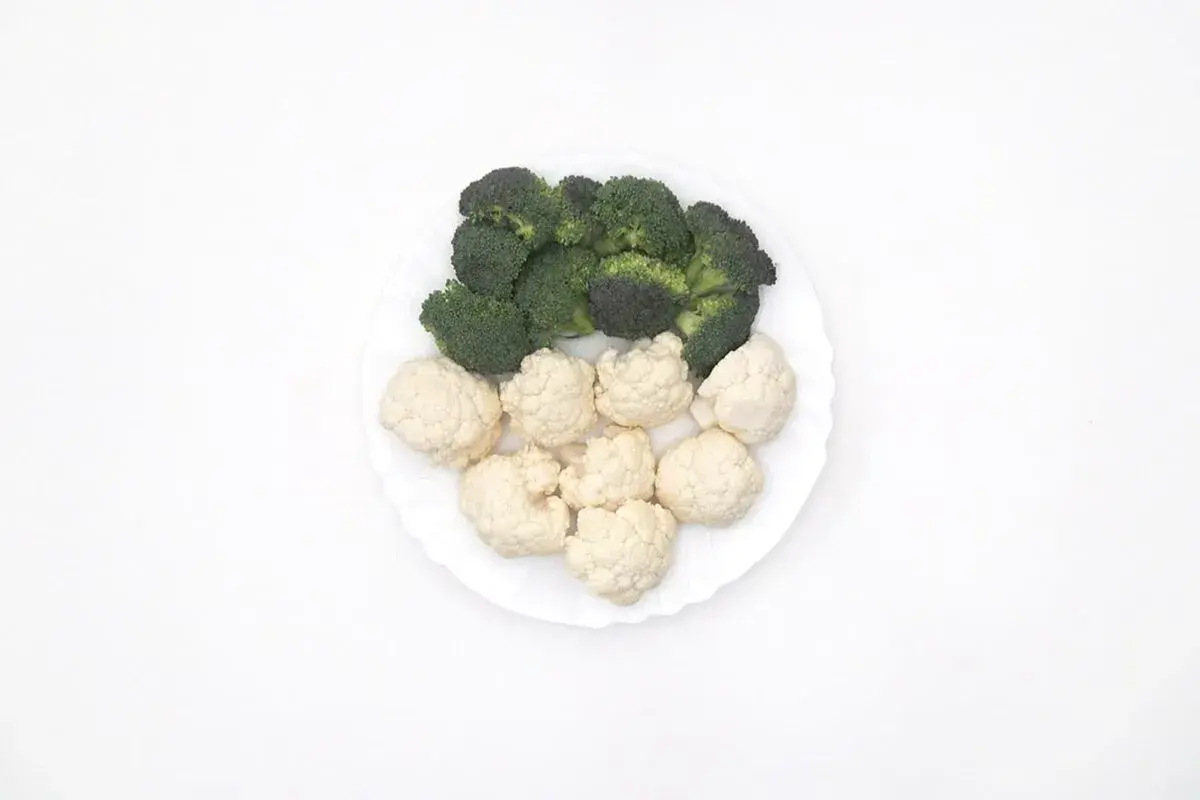 Un plato blanco con un panache de verduras: brócoli verde y coliflor blanca, listos para cocinar.