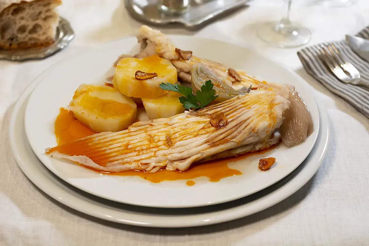 Raya a la gallega servida con patatas cocidas y un toque de ajo frito.