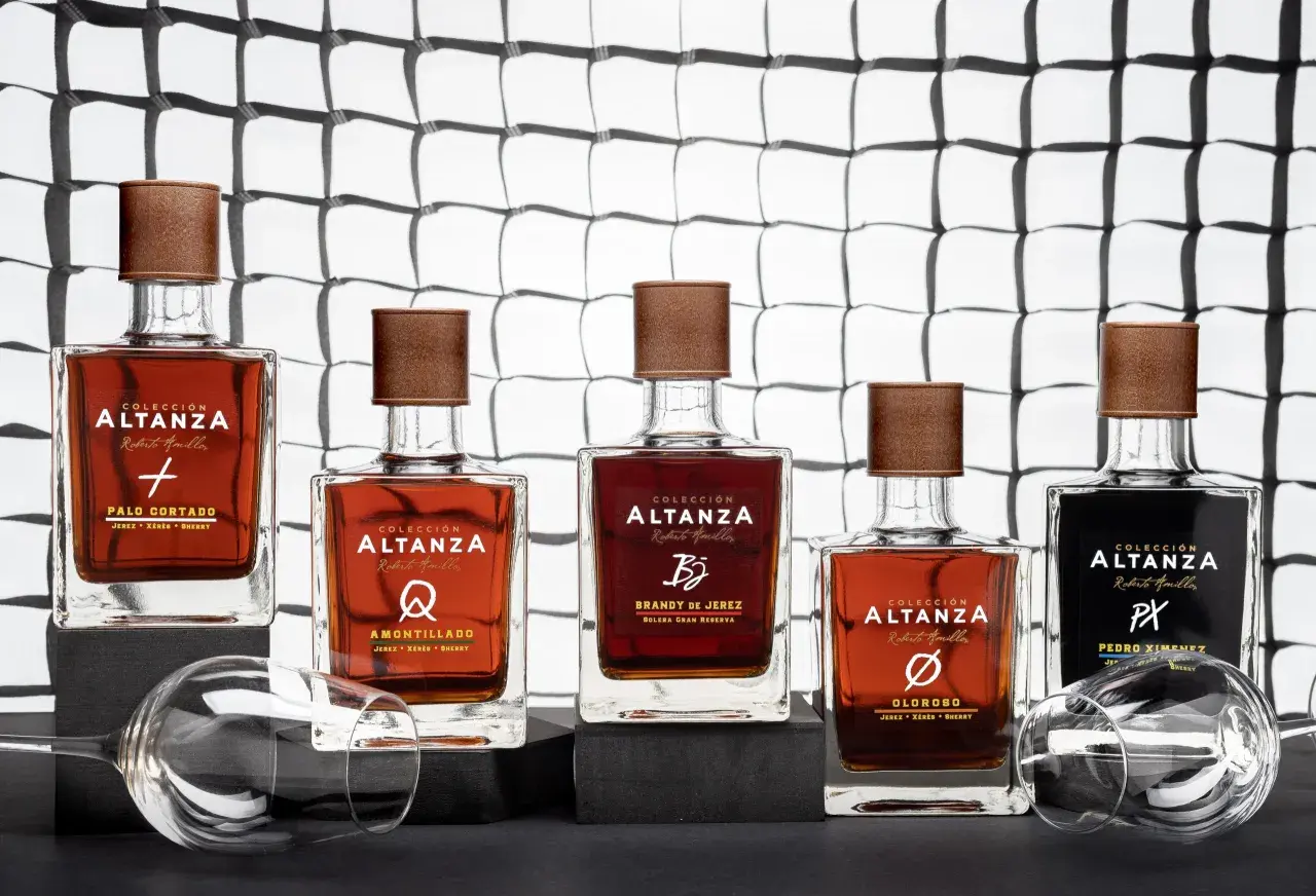 Cinco botellas de brandy de Jerez de la colección Altanza, incluyendo un amontillado, dispuestas sobre una superficie oscura con copas de vino vacías.