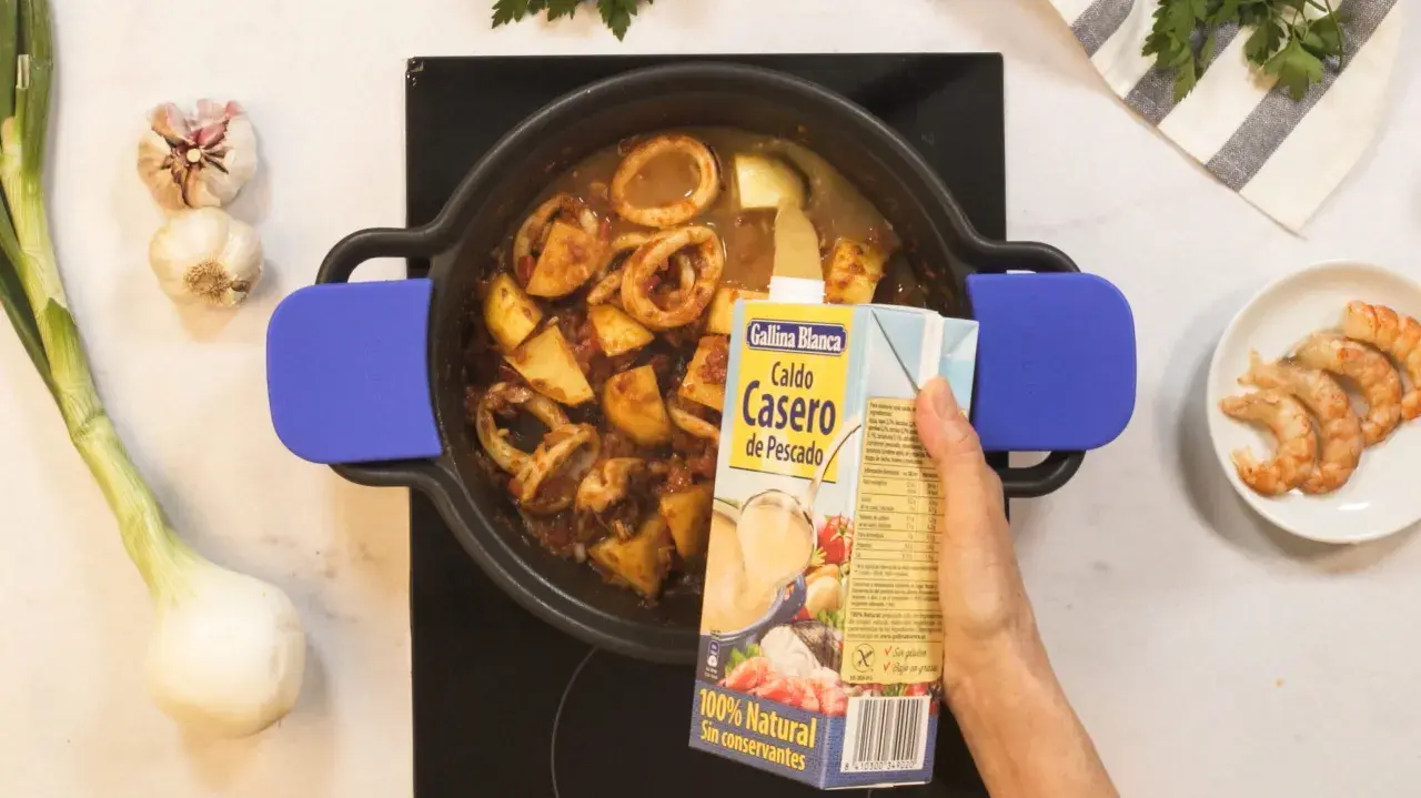 Se añade caldo de pescado a una cazuela con calamares y patatas, ingredientes para una deliciosa caldereta.