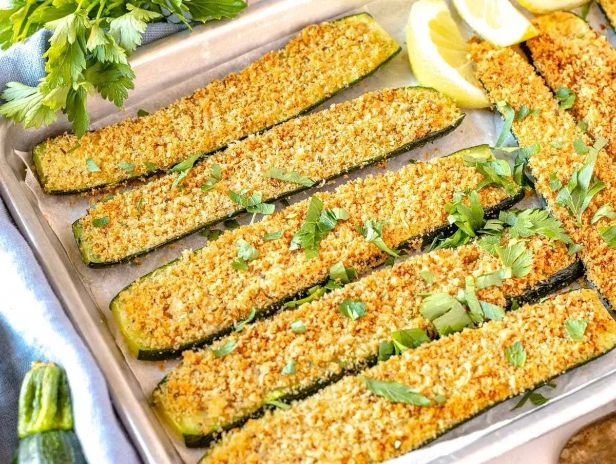 Calabac&iacute;n al horno crujiente, cortado en bastones y espolvoreado con pan rallado y perejil fresco. Servido con gajos de lim&oacute;n.
