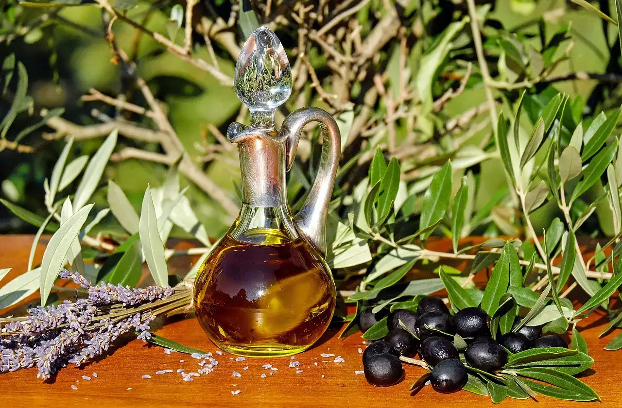 Aceite de oliva en una aceitera de plata, junto a aceitunas y lavanda, mostrando los usos del olivo en la cocina y aromaterapia.