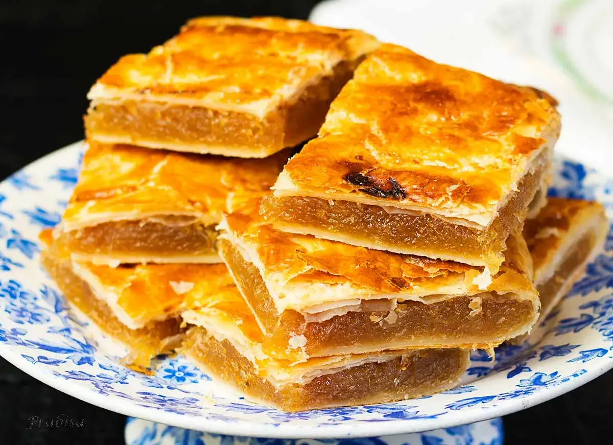 Porci&oacute;n de pastel cordob&eacute;s, con su masa dorada y relleno dulce, apilado en un plato con dise&ntilde;o floral azul.