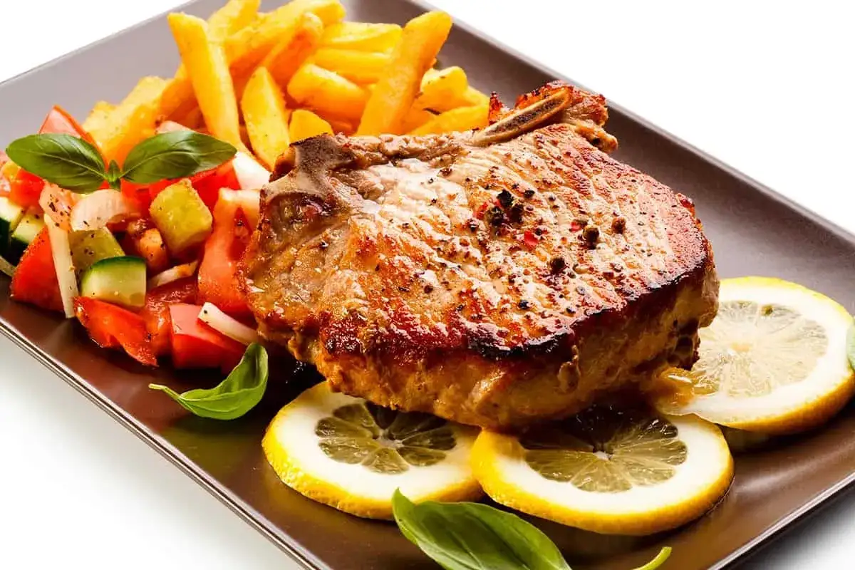 Chuletas de cerdo al horno jugosas, acompa&ntilde;adas de papas fritas crujientes, ensalada fresca y rodajas de lim&oacute;n.