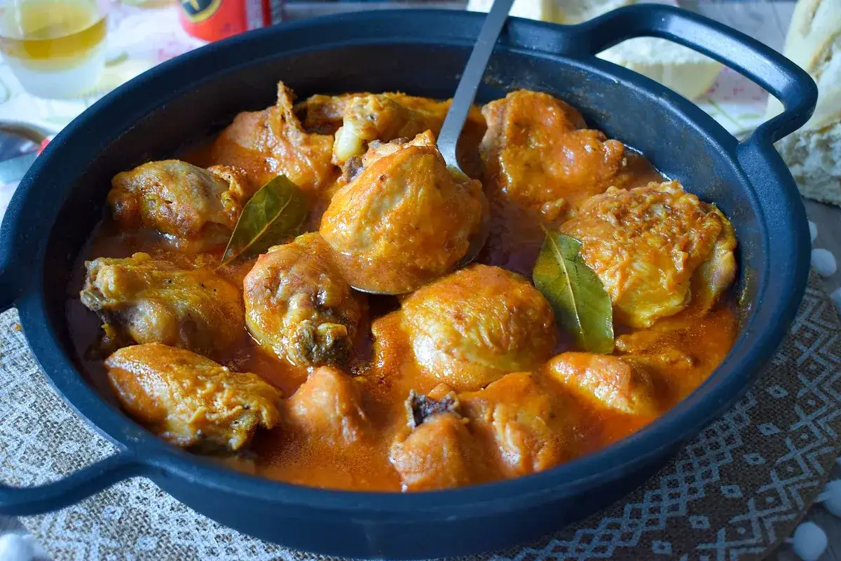Sabroso pollo a la cerveza, cocinado a fuego lento en una cazuela de hierro fundido con una rica salsa anaranjada y hojas de laurel.