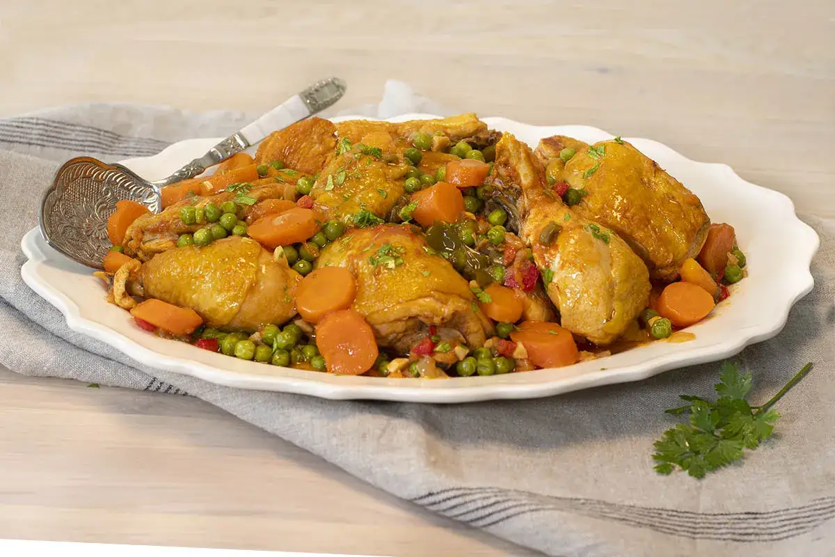 Sabroso pollo al chilindr&oacute;n con guisantes y zanahorias en una fuente blanca, listo para servir.
