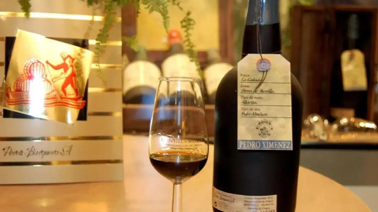 Botella de vino Pedro Xim&eacute;nez y copa con vino dulce, mostrando c&oacute;mo se hace el vino dulce.