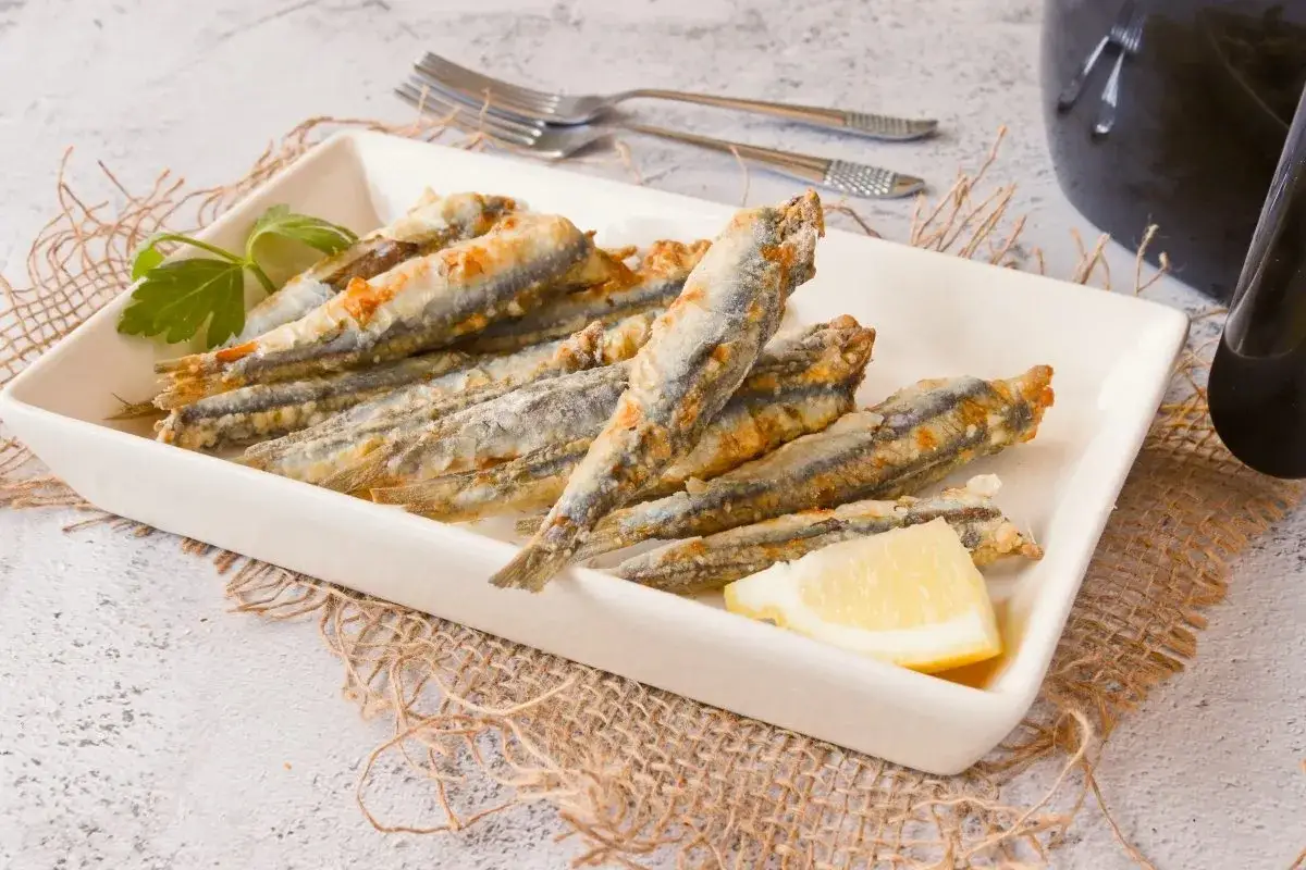 Boquerones en freidora de aire, dorados y crujientes, servidos en plato blanco con lim&oacute;n y perejil. &iexcl;Un aperitivo saludable y delicioso!