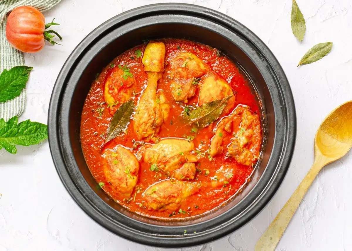 Sabroso pollo con tomate cocinado a fuego lento, con trozos de pollo dorados en una rica salsa roja, adornado con perejil fresco y hojas de laurel.