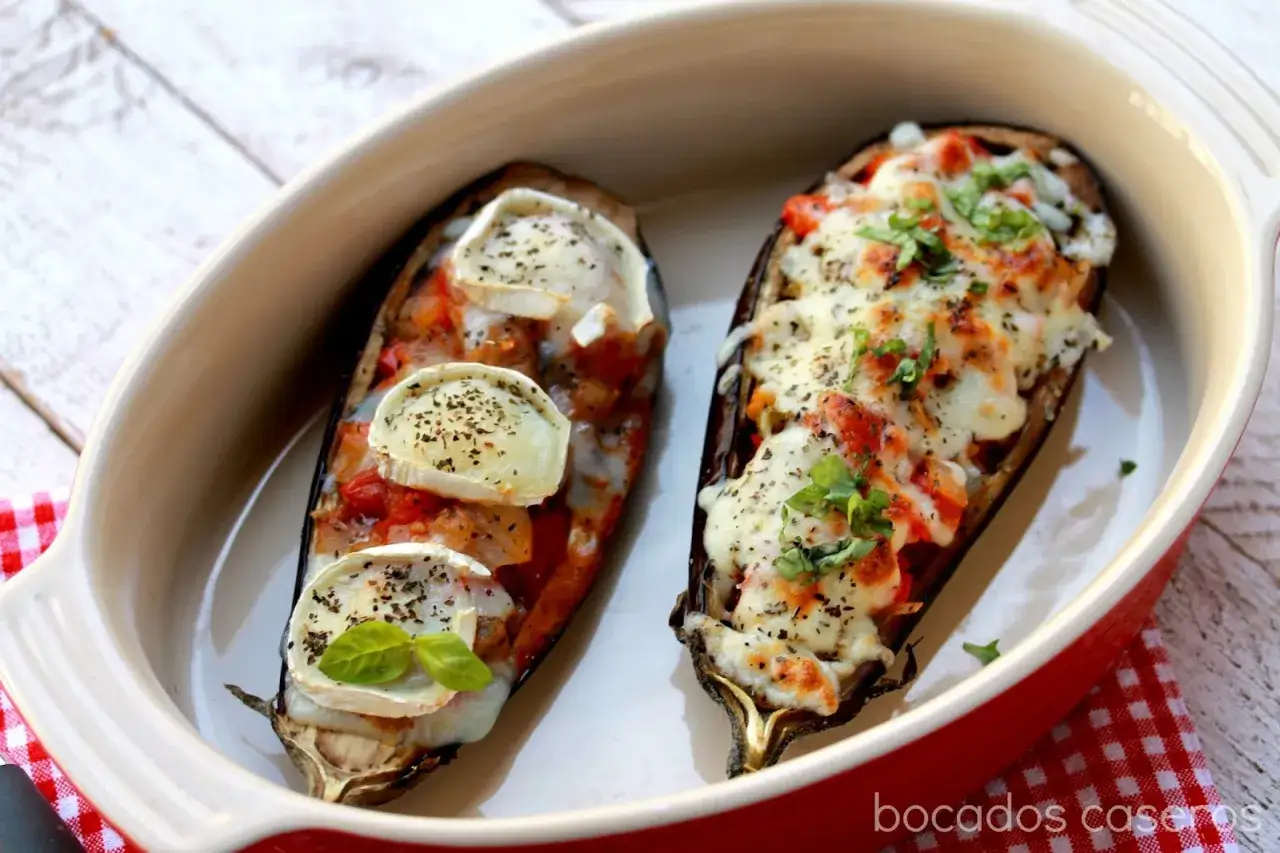 Dos mitades de berenjenas rellenas, una con queso de cabra y hierbas, la otra gratinada con queso fundido y tomate. &iexcl;Deliciosas berenjenas rellenas!