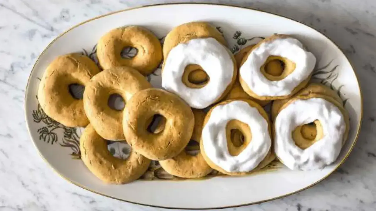 Rosquillas tontas doradas y algunas cubiertas con glaseado blanco, dispuestas en una bandeja decorada.