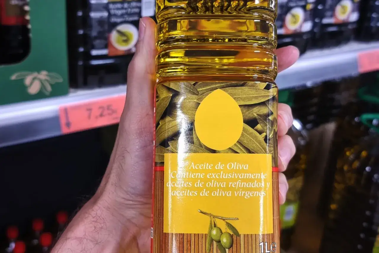 Una mano sostiene una botella de aceite de oliva. La etiqueta indica que contiene aceites de oliva refinados, que son malos para la salud.