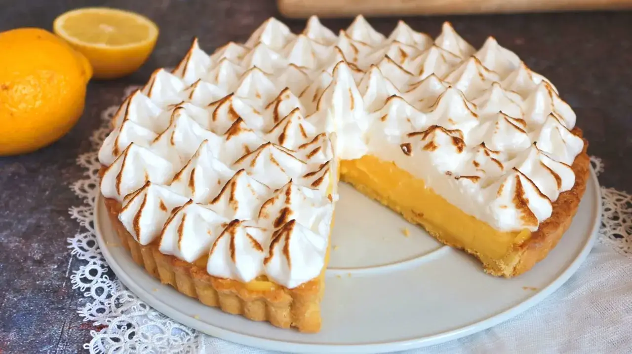 Tarta de lim&oacute;n con merengue tostado, con una porci&oacute;n retirada para mostrar el relleno cremoso.