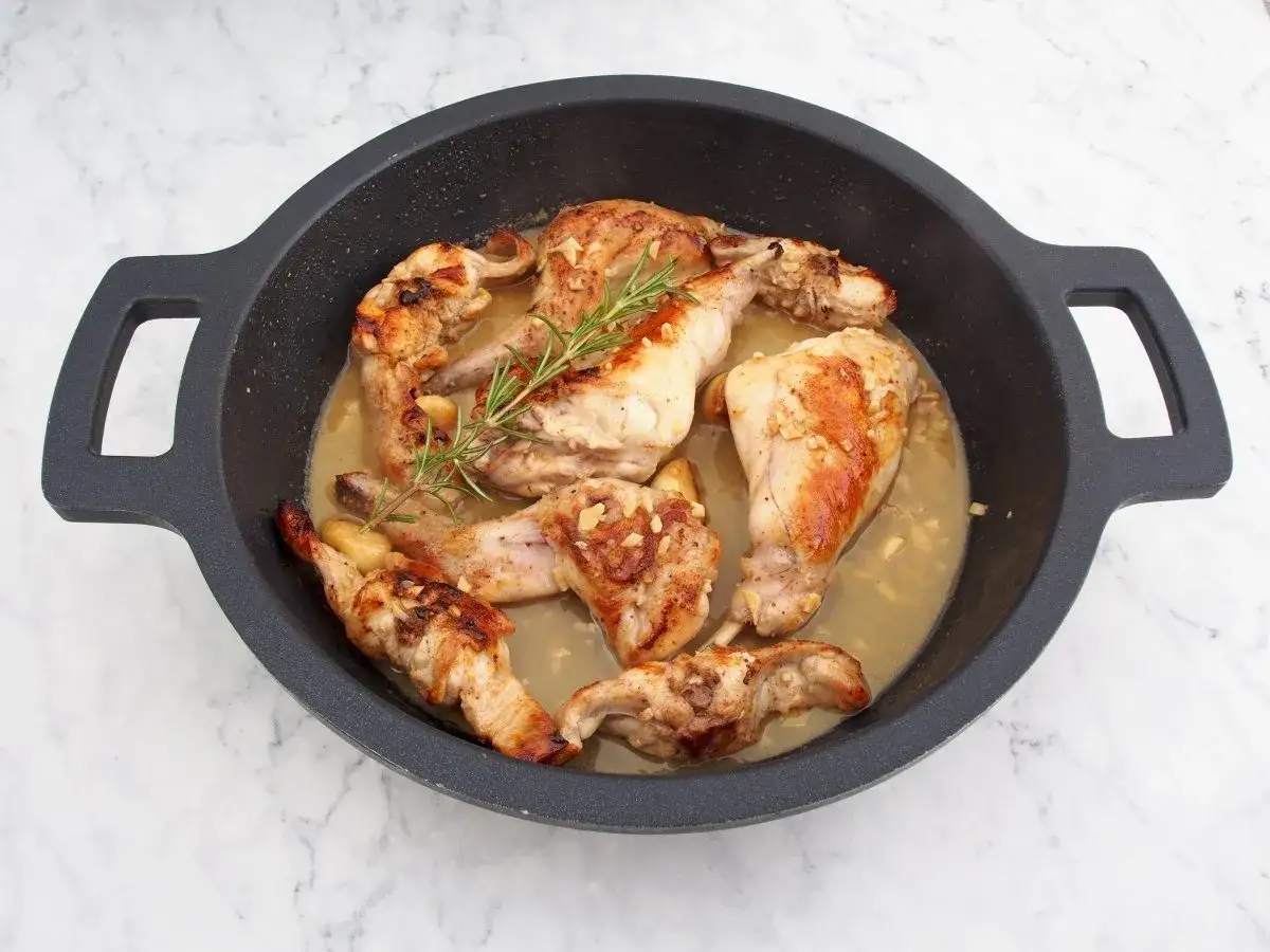 Sabroso conejo al ajillo en una sart&eacute;n, con trozos dorados de carne, ajo picado y una ramita de romero fresco.