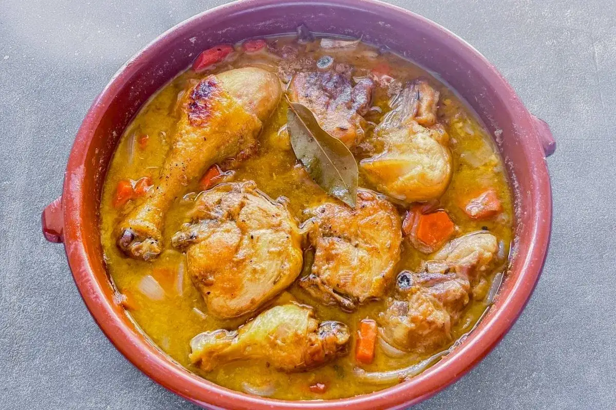 Delicioso pollo en salsa dorada, con trozos de zanahoria y cebolla, servido en una cazuela de barro. ¡Un plato casero que huele increíble!