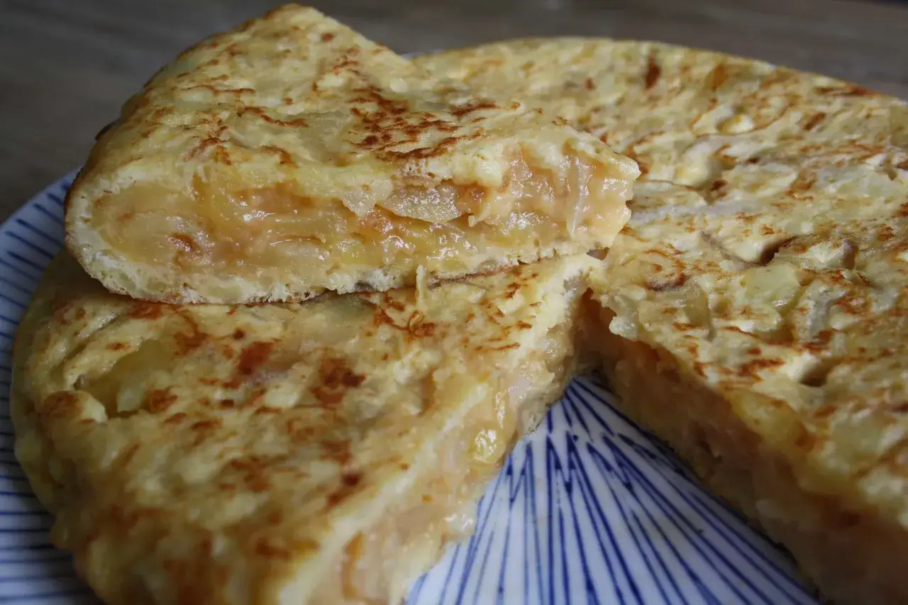 Una jugosa tortilla de patatas, con trozos de patata tierna y huevo dorado, servida en un plato con rayas azules.