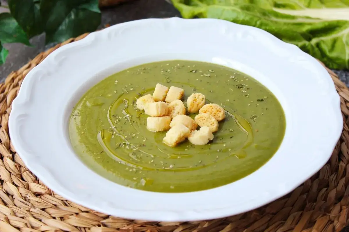 Crema de acelgas servida en plato blanco, decorada con picatostes y un chorrito de aceite de oliva.