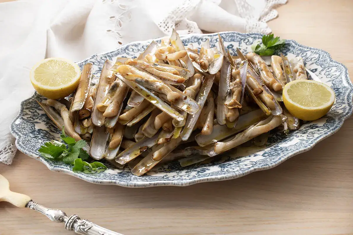 Deliciosas navajas a la plancha servidas en una fuente con limón y perejil.