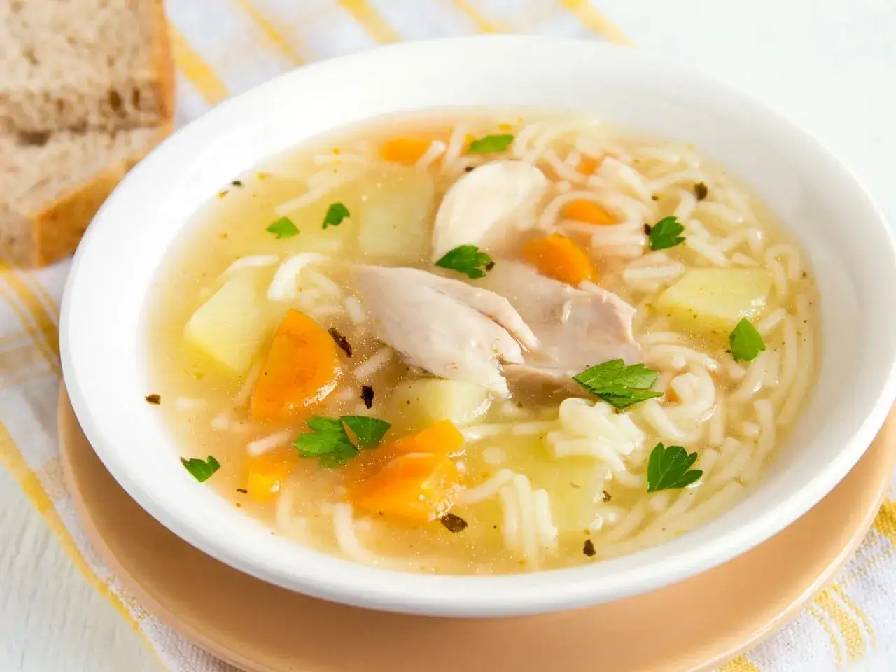 Un reconfortante plato de sopa de fideos con pollo, zanahoria y patata, adornado con perejil fresco.
