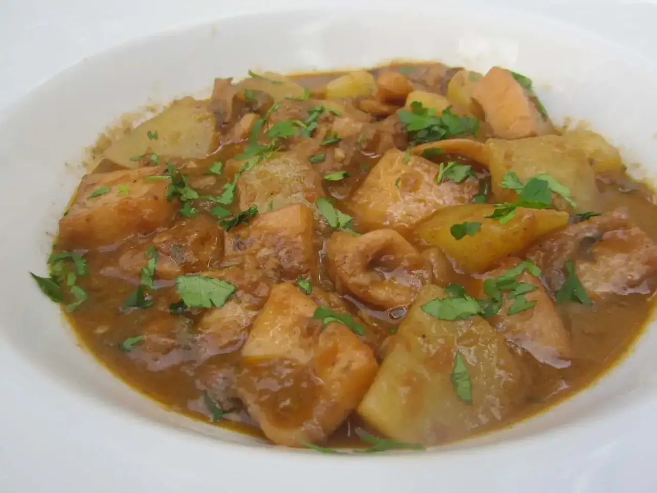 Un plato de sepia con patatas, troceada y guisada en una salsa sabrosa, adornado con perejil fresco.