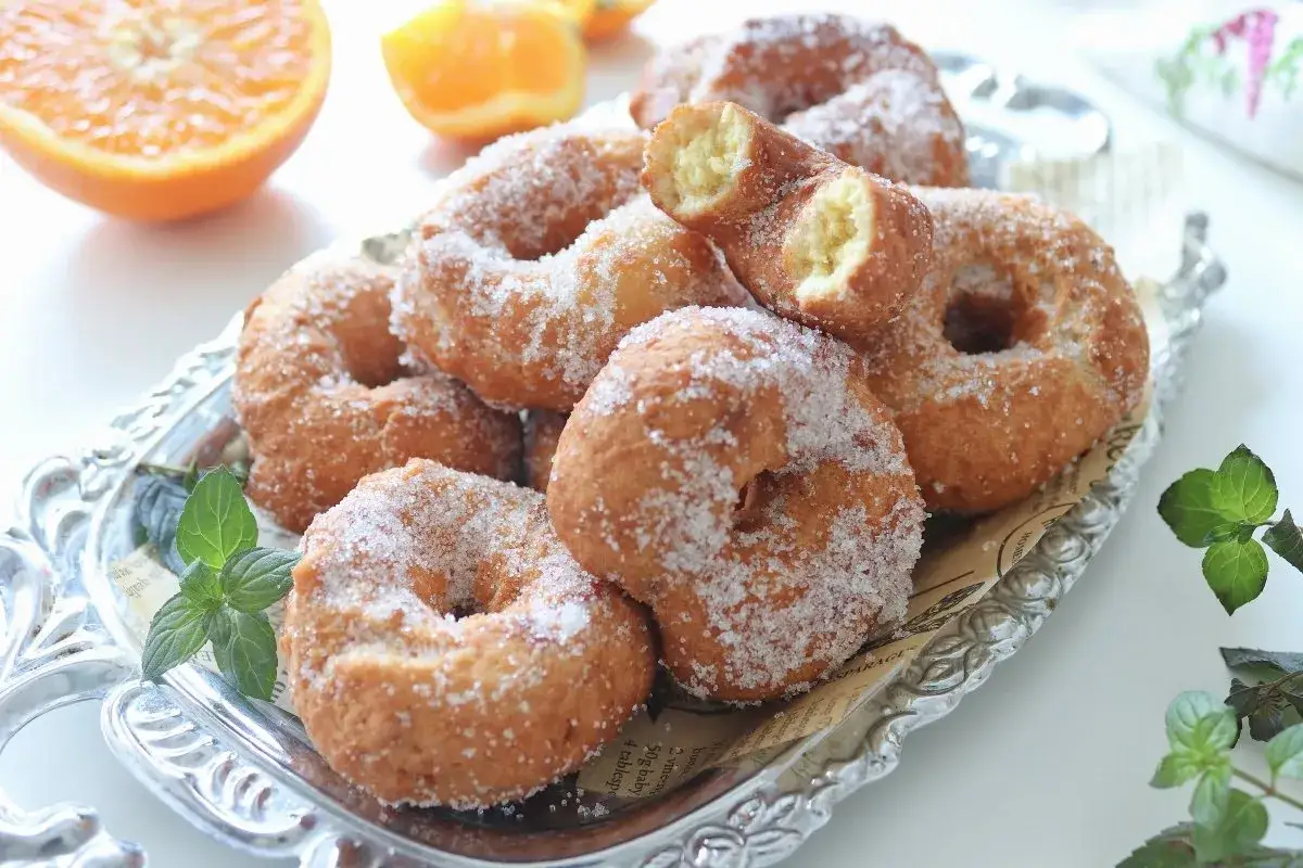 Rosquillas de naranja recién hechas, cubiertas de azúcar, servidas en una bandeja plateada con hojas de menta.