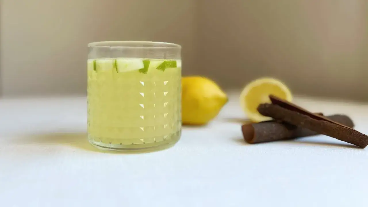 Vaso con refrescante leche merengada, adornado con trozos de manzana. Limones y canela en rama al fondo.