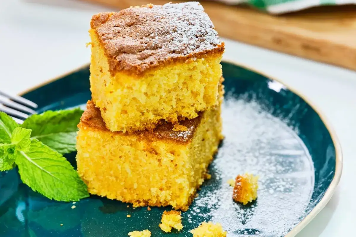 Dos porciones de bizcocho de calabaza espolvoreadas con az&uacute;car glas, acompa&ntilde;adas de hojas de menta fresca en un plato azul.