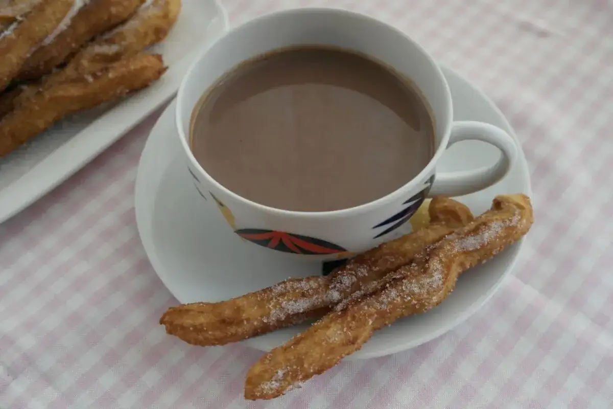 Churros caseros recién hechos, espolvoreados con azúcar, junto a una taza de chocolate caliente.