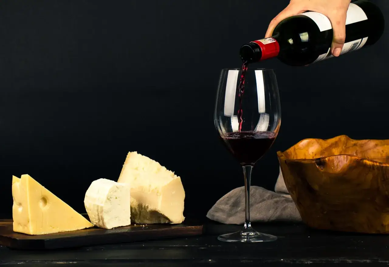 Vino tinto sirvi&eacute;ndose en copa, acompa&ntilde;ado de quesos y un cuenco de madera. Un deleite que evoca la experiencia de un vino amontillado.