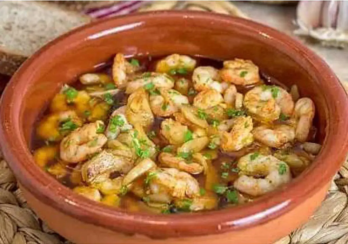 Tazón de barro con gambas al ajillo, cubiertas de perejil picado y aceite burbujeante.