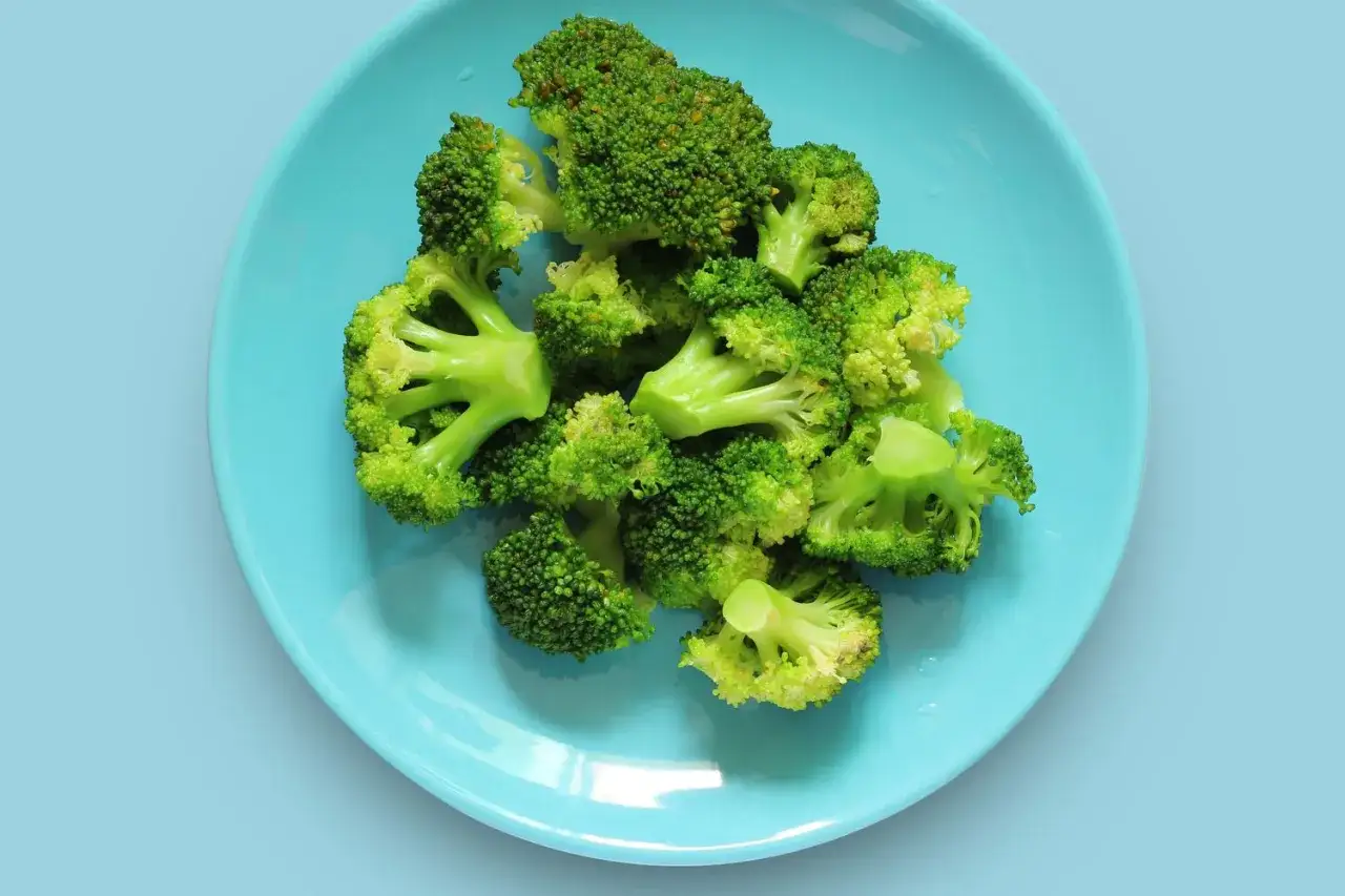 Brotes de br&oacute;coli reci&eacute;n cocidos, listos para comer, en un plato azul brillante.