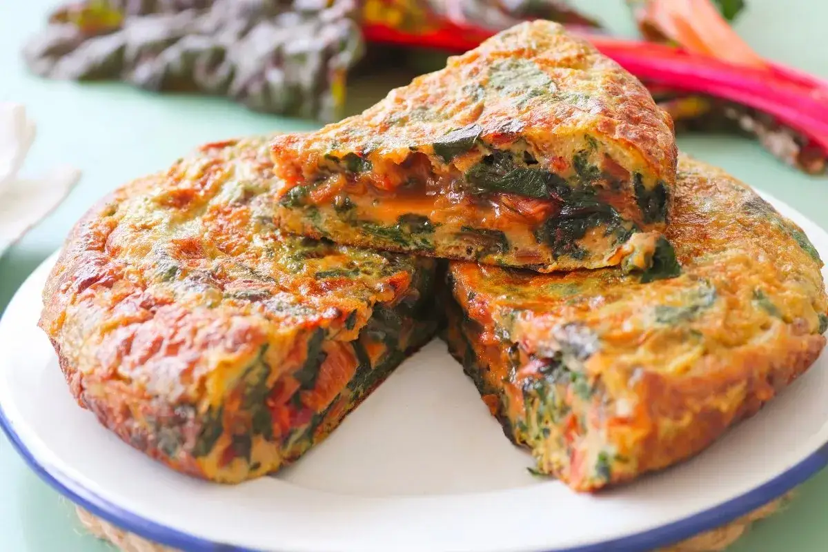Tortilla de acelgas jugosa y dorada, con trozos de verdura y un interior apetitoso.