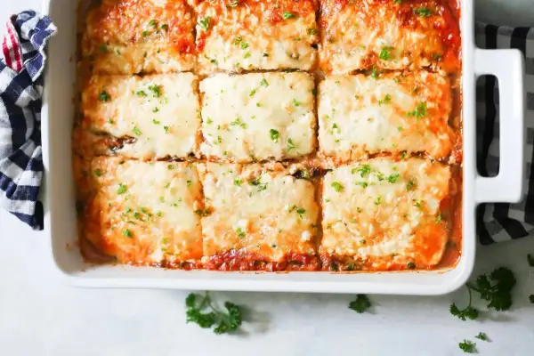 Lasaña de berenjena recién horneada, cubierta de queso derretido y perejil fresco, lista para servir.