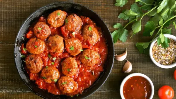 Sabrosas albóndigas en salsa roja, servidas en una sartén de hierro fundido, con perejil fresco y especias al lado.